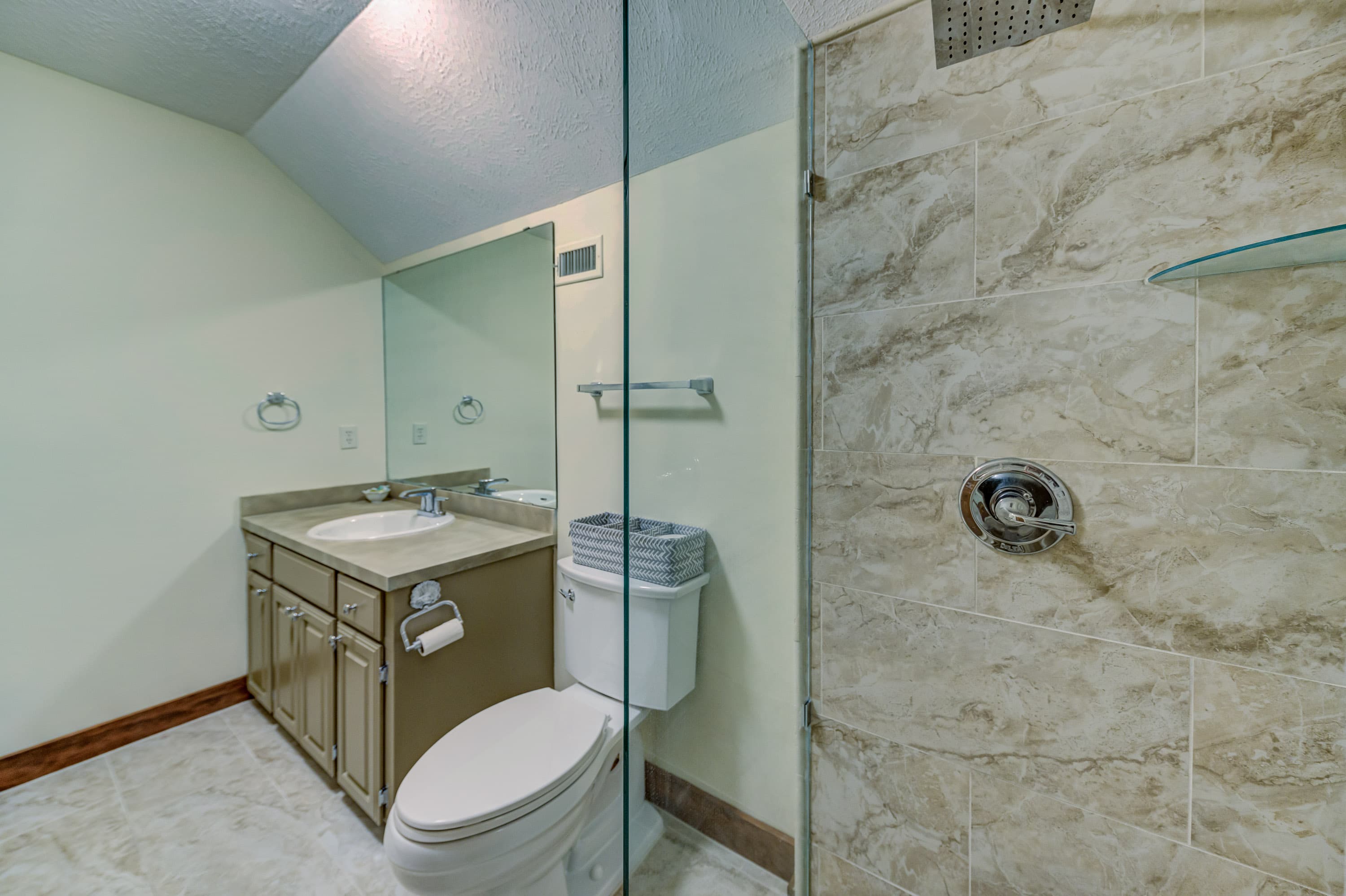 A modern bathroom featuring a glass shower, sink with cabinet, toilet, and mirror.