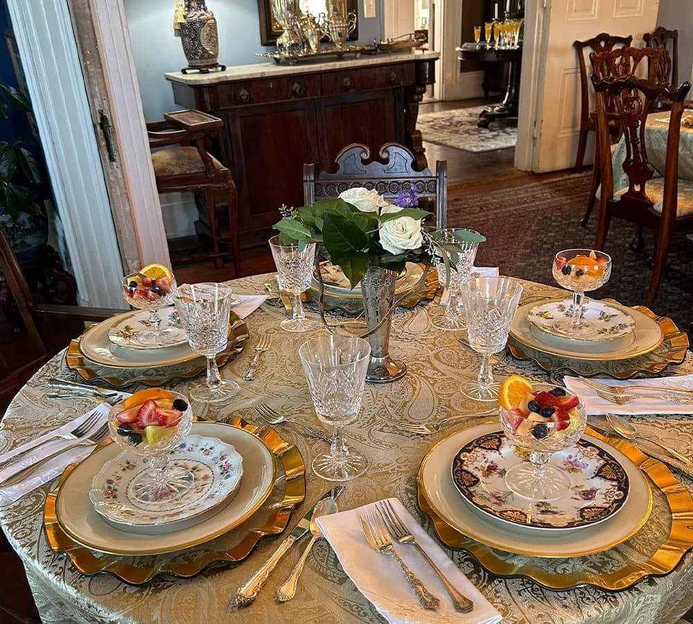 A beautifully set dining table featuring elegant dishware, crystal glasses, and bowls of fresh fruit.