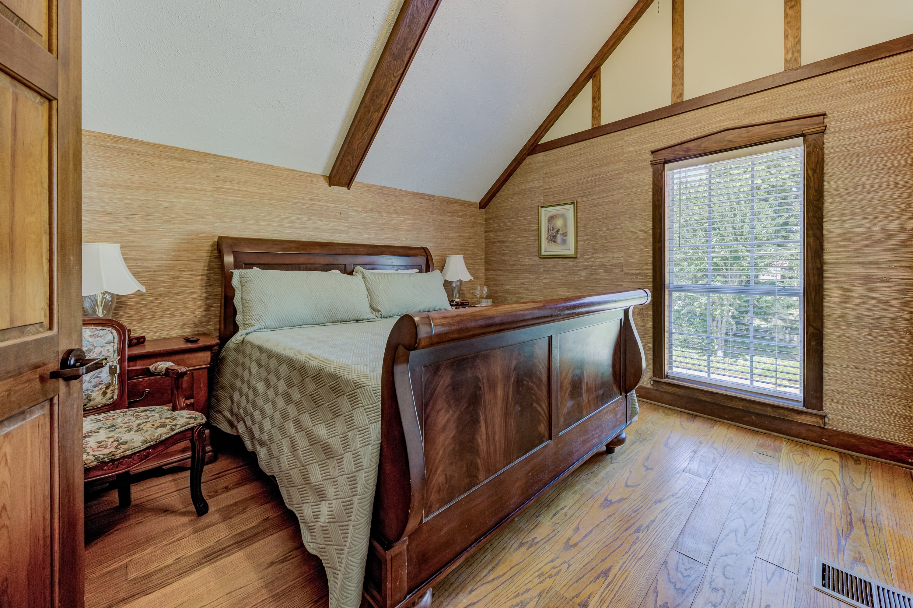 Cozy bedroom featuring a wooden sleigh bed, bedside tables with lamps, and large windows with natural light.