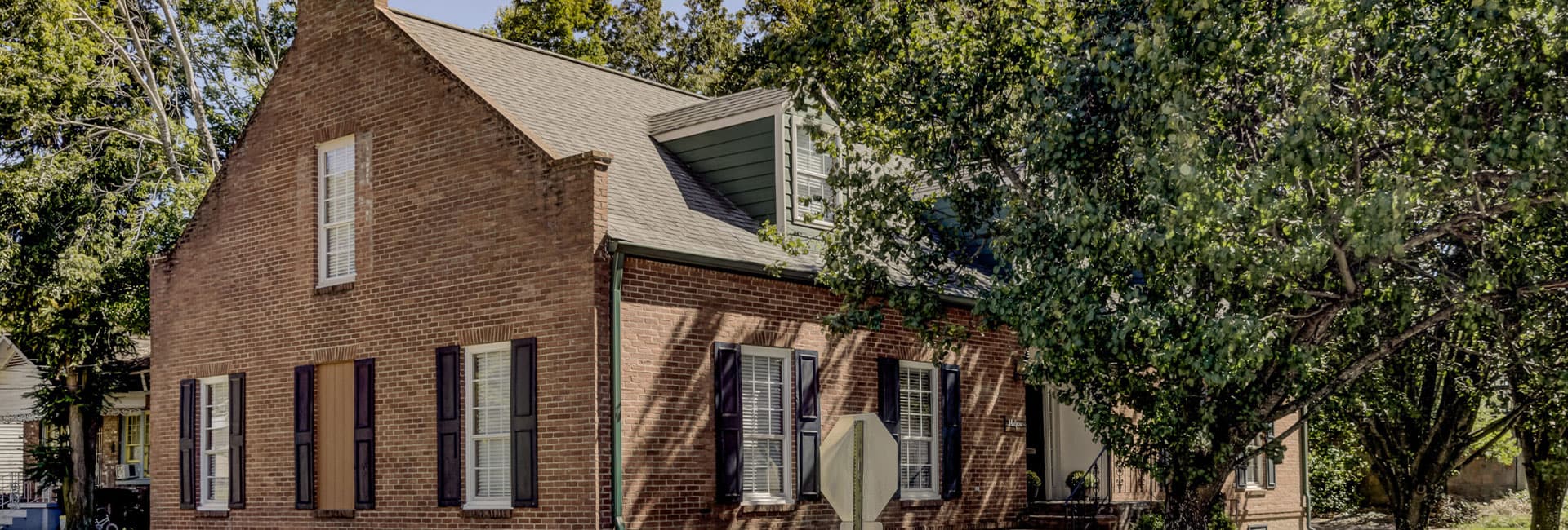 A brick house with a sloped roof, surrounded by trees.