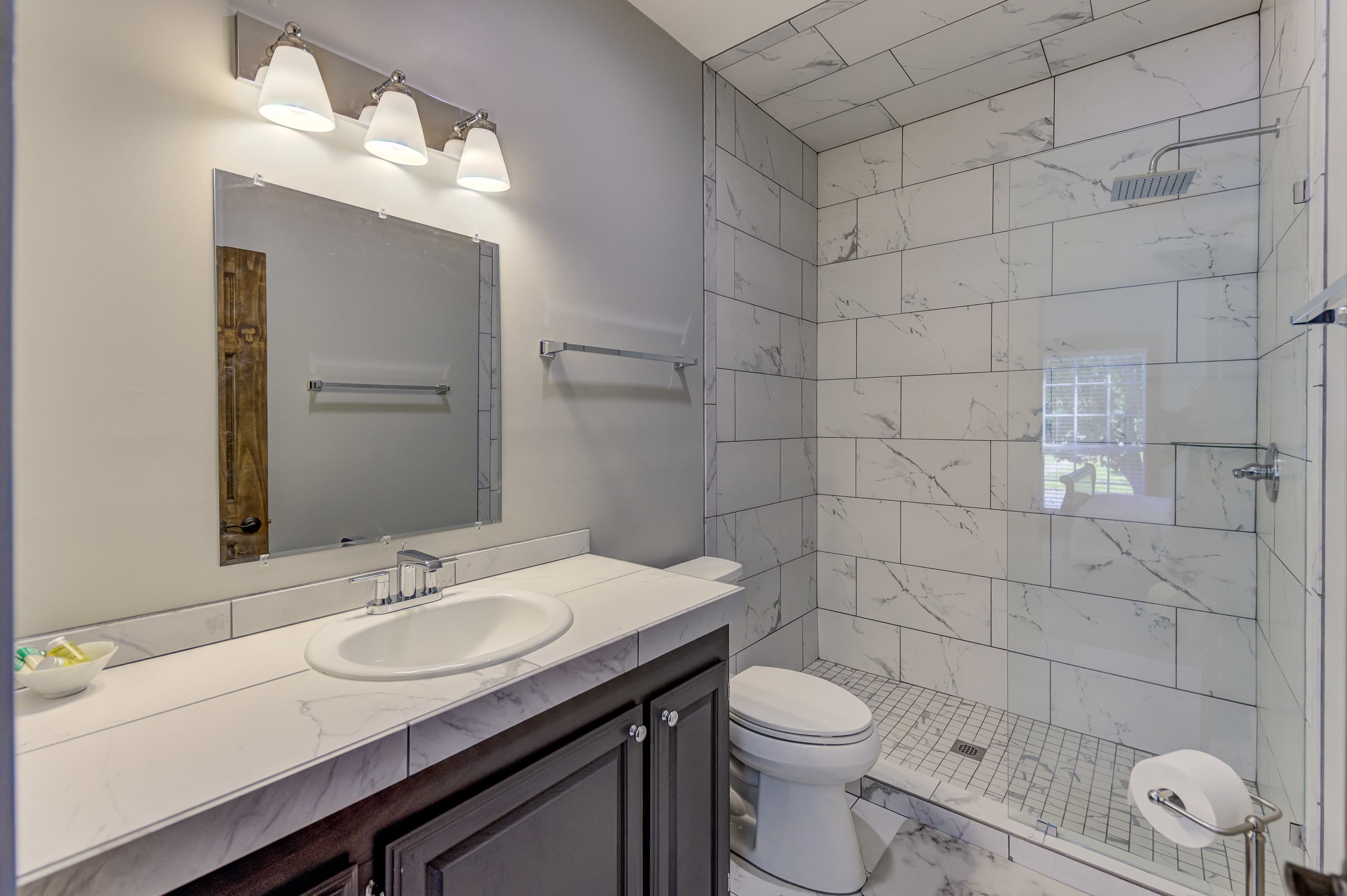 A modern bathroom featuring marble tiles, a spacious shower, and a sleek vanity.