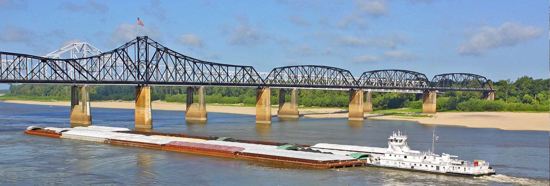 A barge navigates the river beneath a steel bridge on a clear day.
