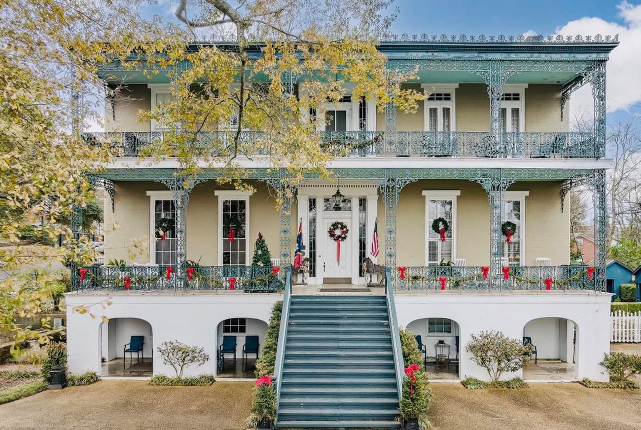 A historic two-story home with a decorative balcony and festive holiday wreaths.