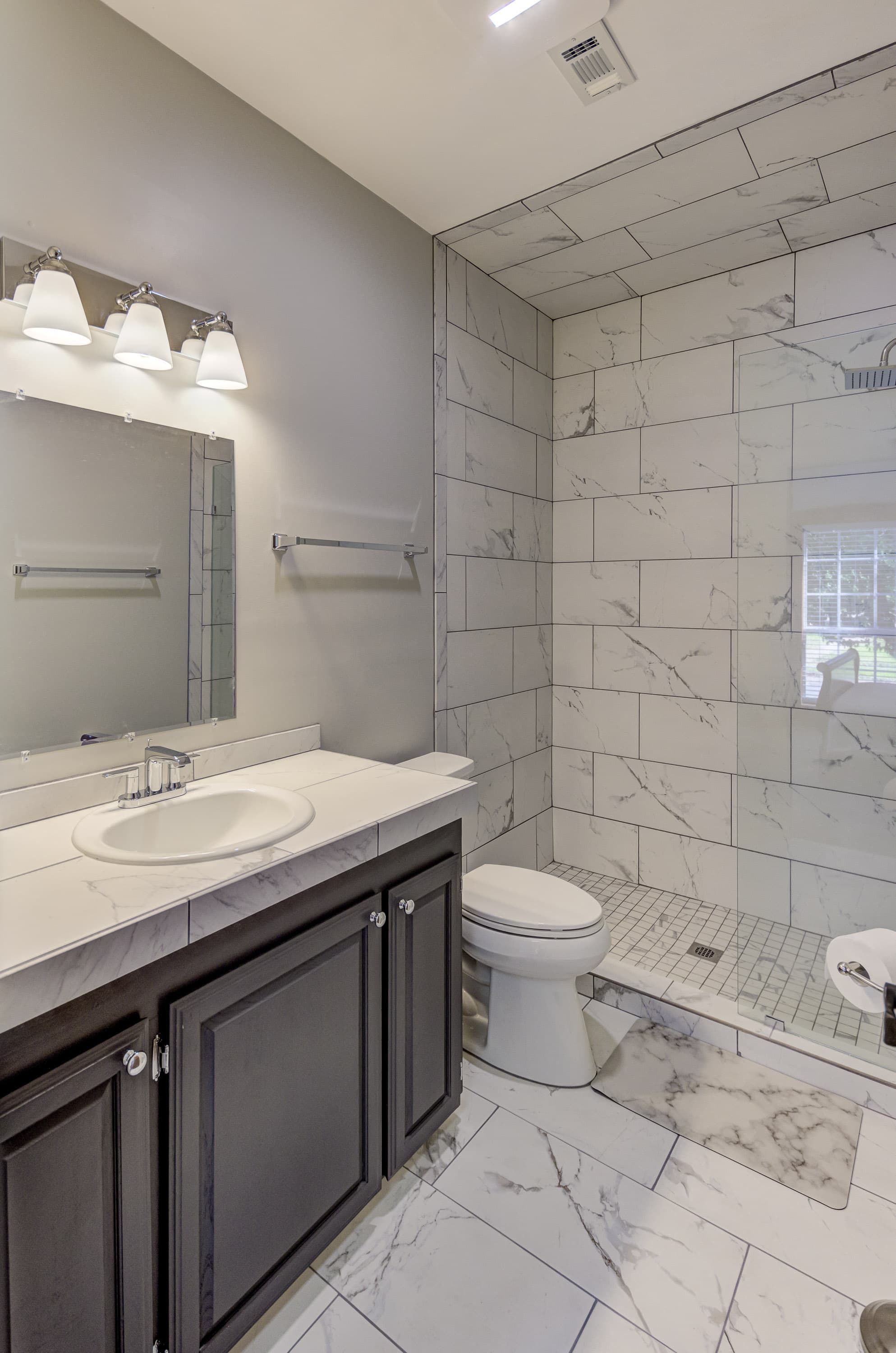 Modern bathroom featuring a sleek marble shower, dark cabinetry, and a large mirror.