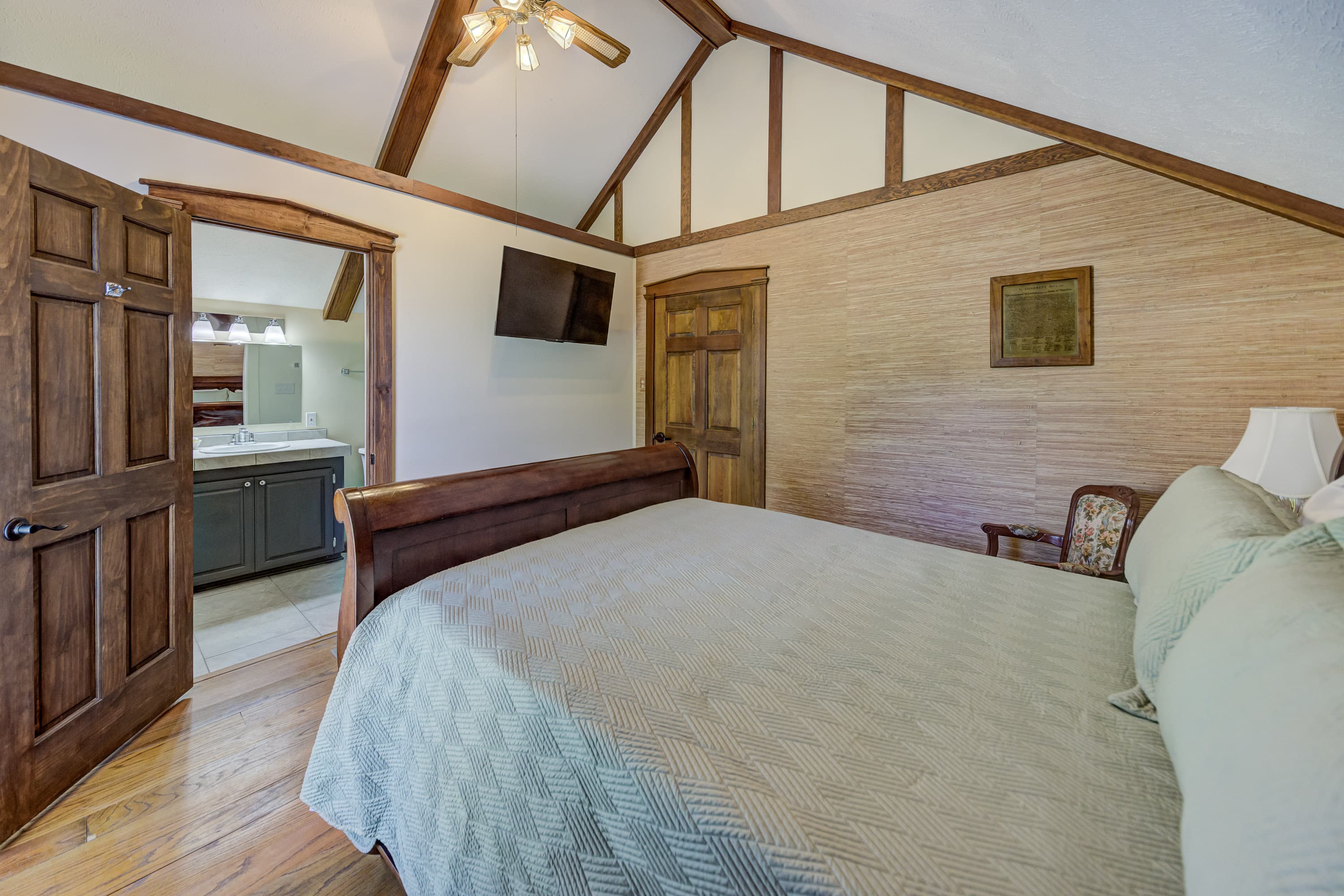 A cozy bedroom featuring a wooden bed, a ceiling fan, and a view of an adjoining bathroom.