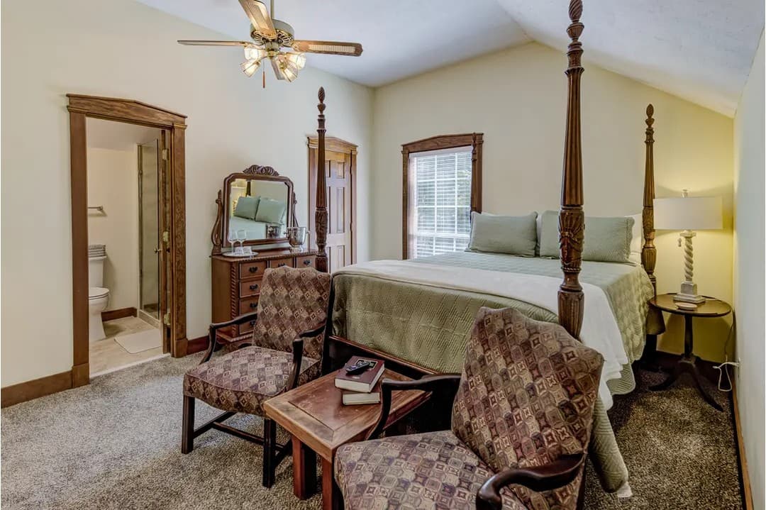 Cozy bedroom featuring a four-poster bed, two chairs, and a private bathroom entrance.