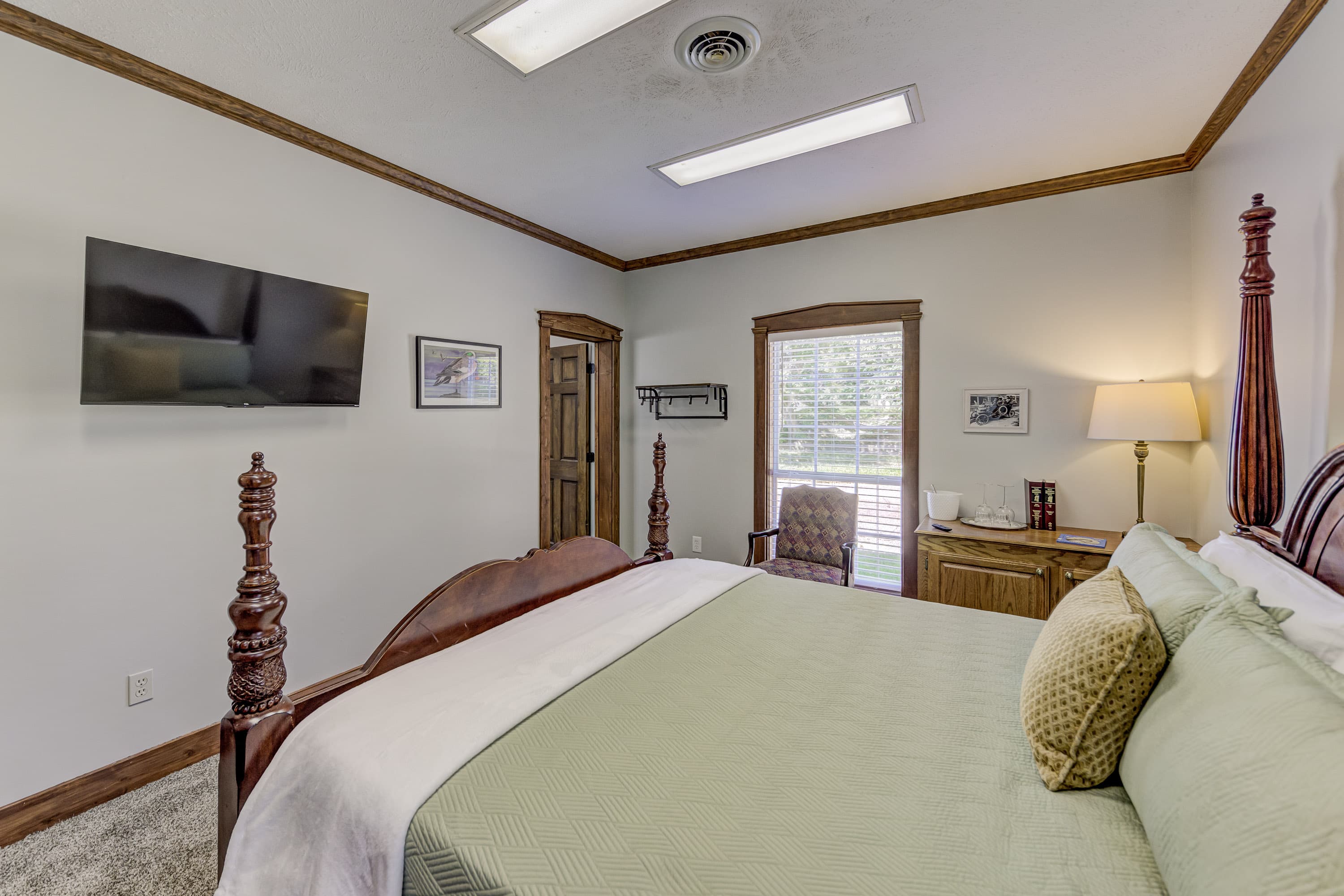 A cozy bedroom featuring a four-poster bed, television, and window with natural light.
