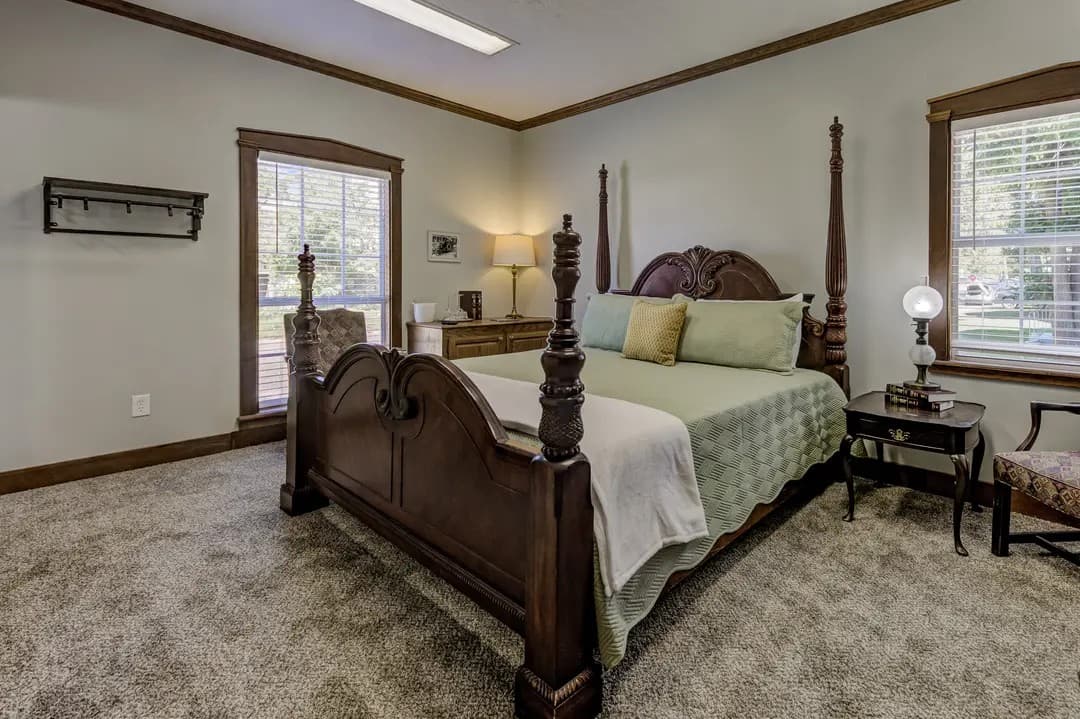 A cozy bedroom featuring a wooden four-poster bed, soft green bedding, and natural light from windows.
