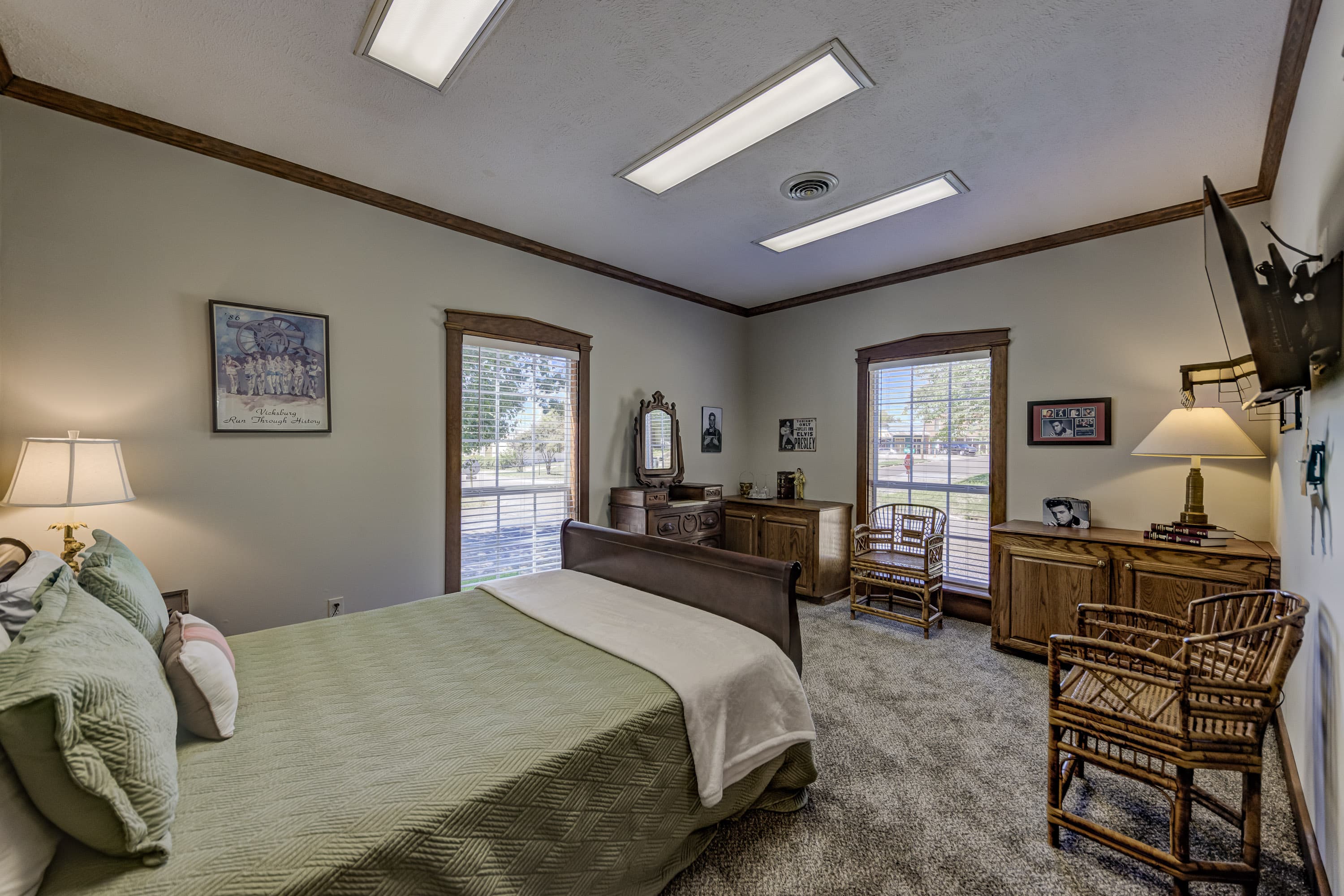 A neatly arranged bedroom featuring a bed, wooden furniture, and large windows allowing natural light.