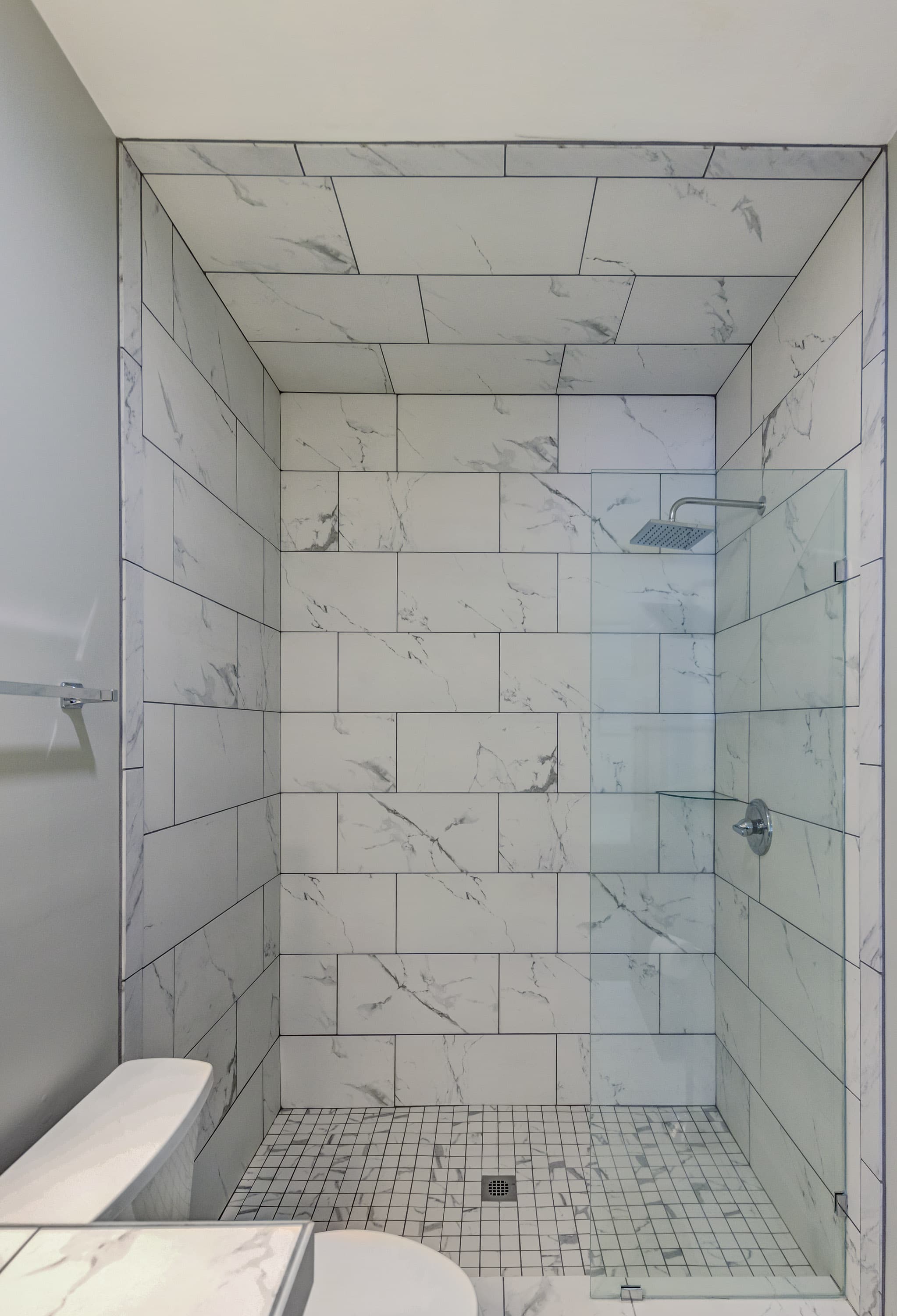 Modern shower with marble tile walls and a glass door.