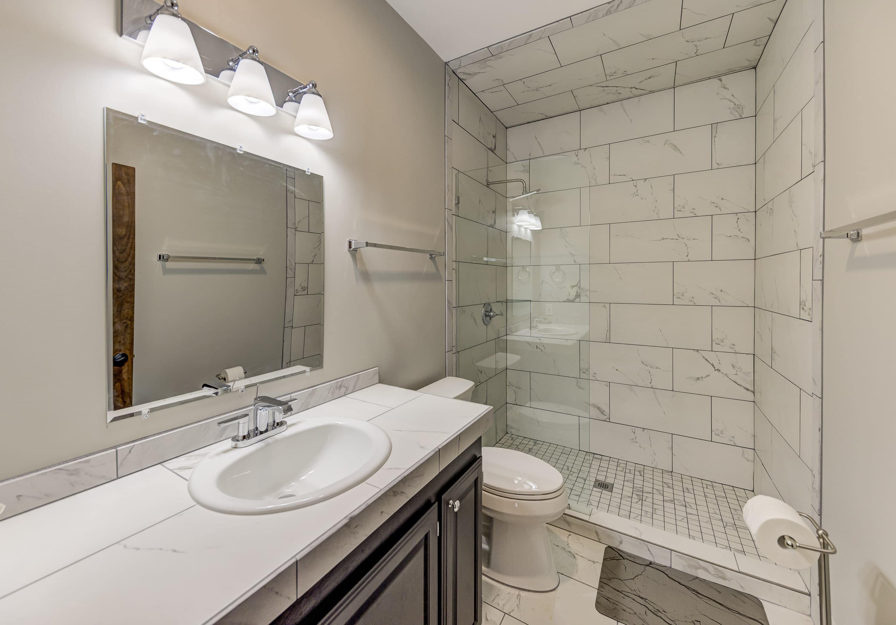 A modern bathroom featuring a glass shower, marble tile, and a dark vanity.