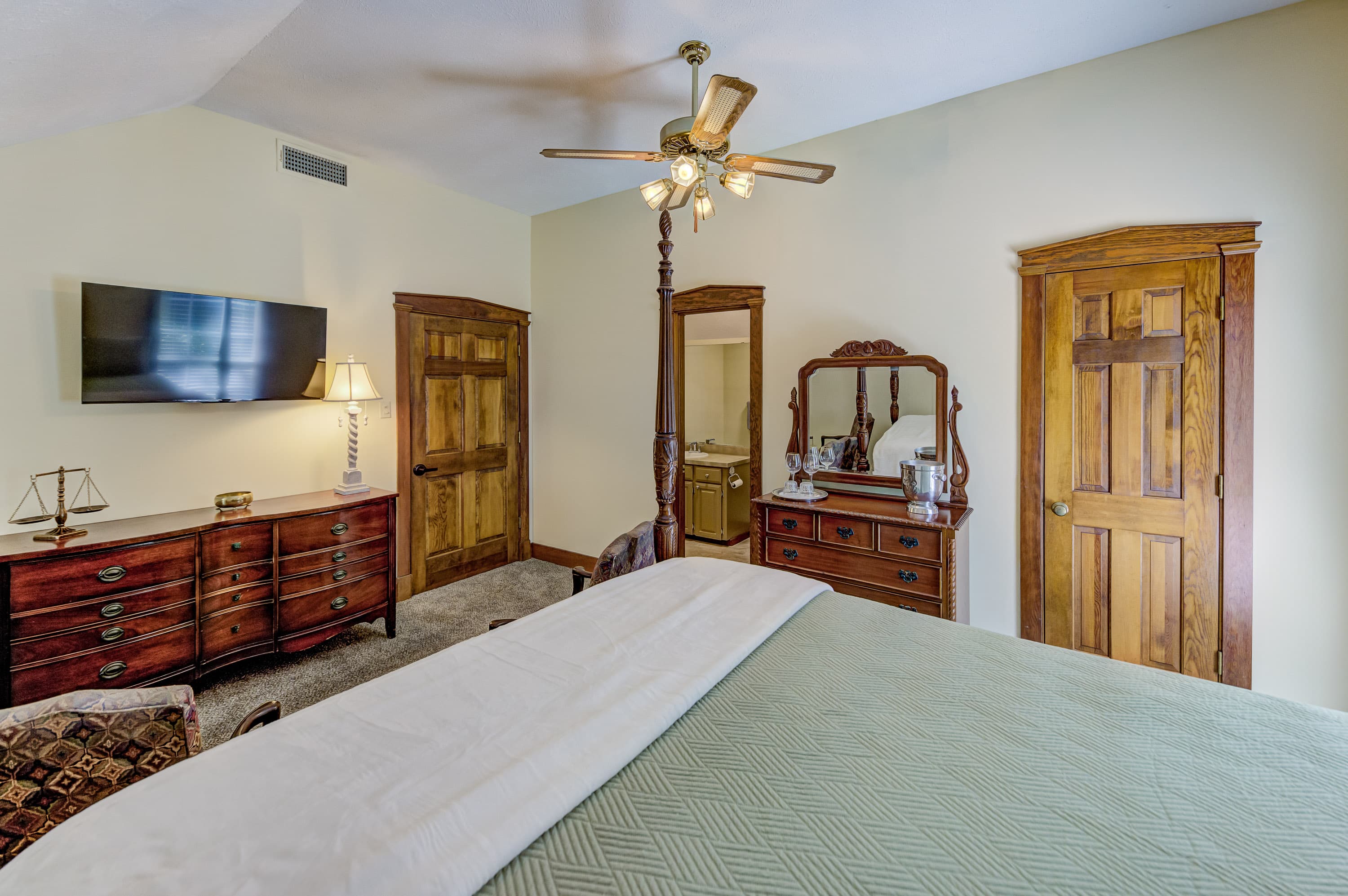 A cozy bedroom featuring a four-poster bed, dresser, TV, and vintage mirrors with wooden doors.
