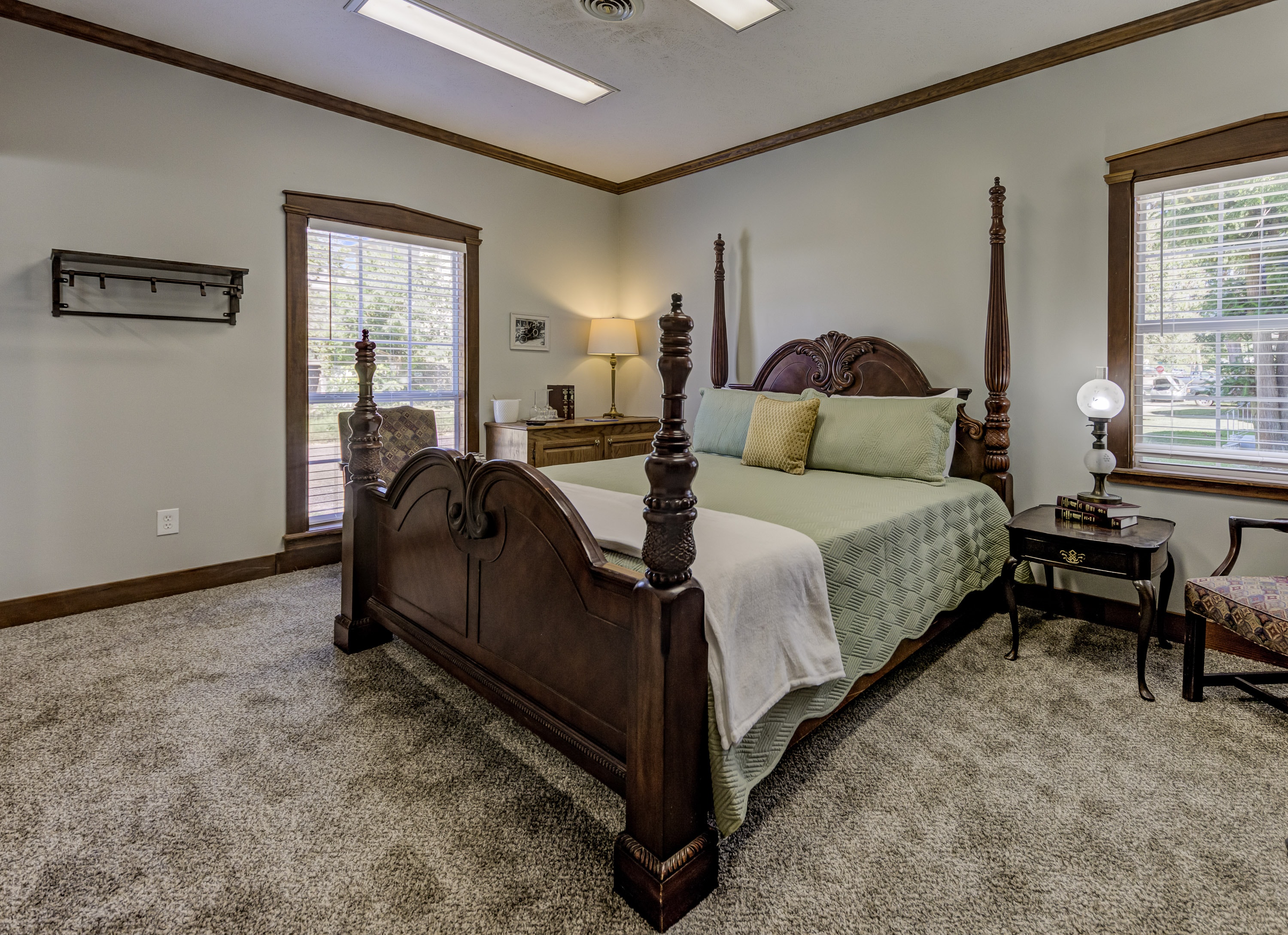 A cozy bedroom featuring a wooden four-poster bed, a bedside table, and large windows letting in natural light.