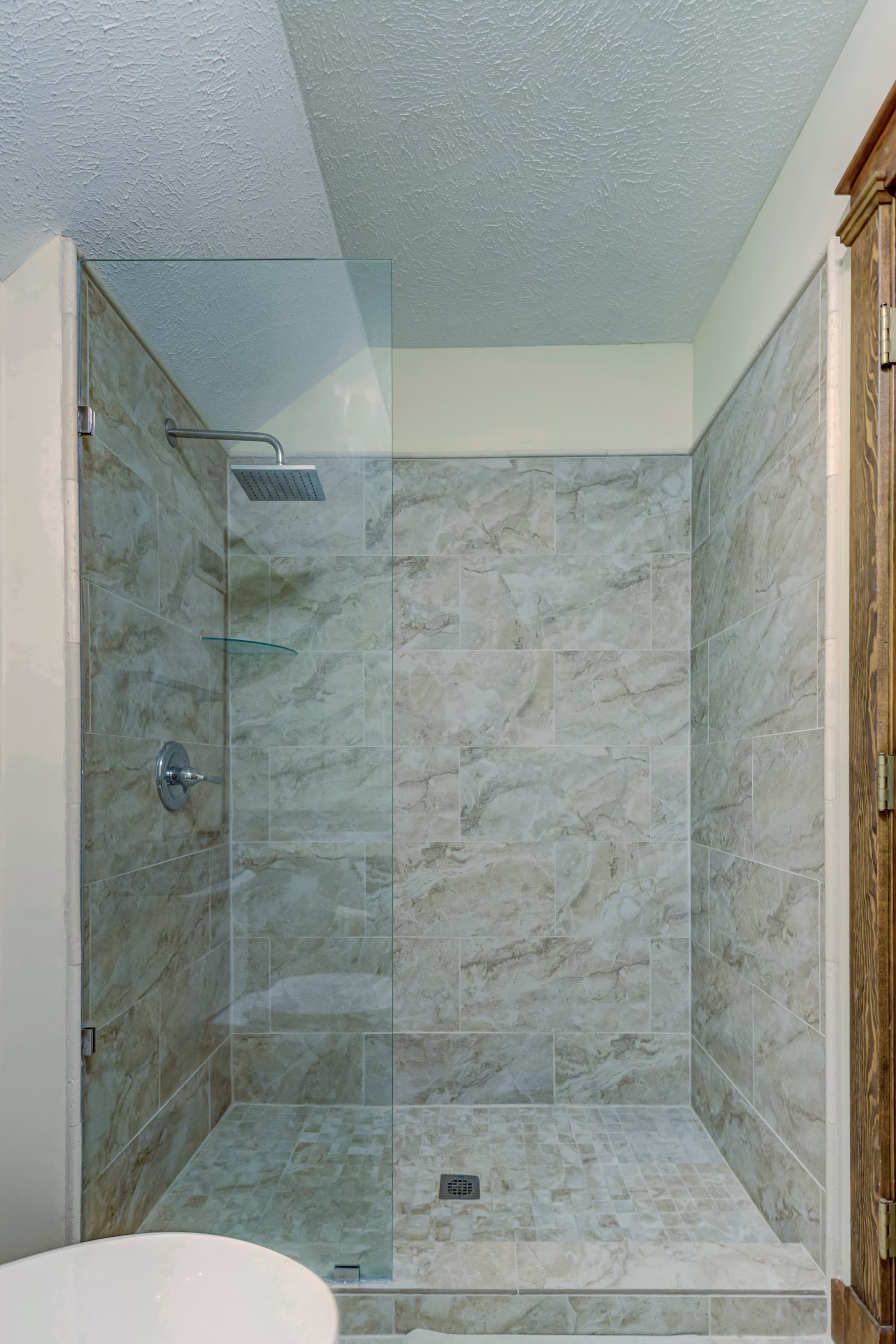 A modern glass shower enclosed by beige stone tiles.