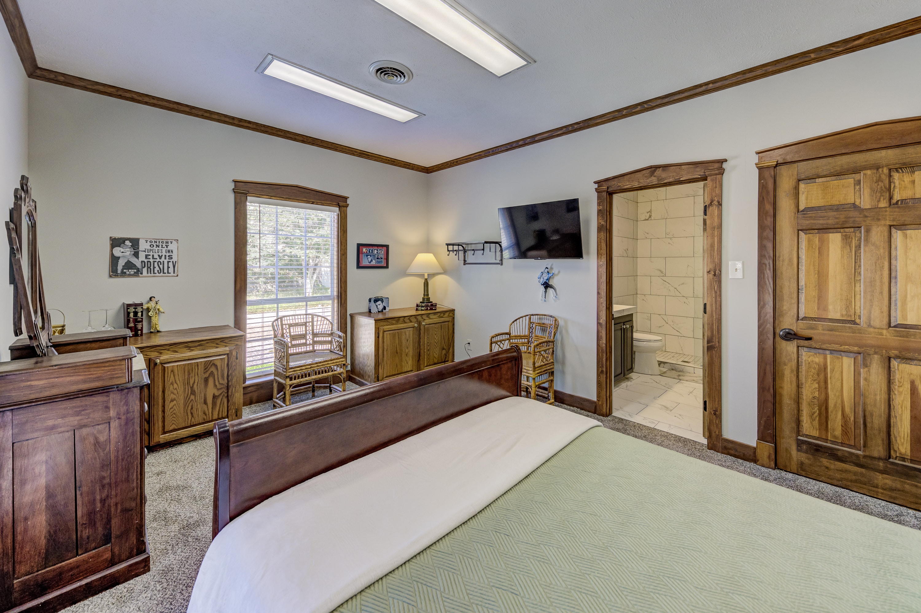 A cozy bedroom featuring a wooden bed, dresser, TV, and an ensuite bathroom.