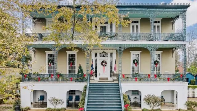 A spacious, two-story house with intricate ironwork features, decorated for the holidays.